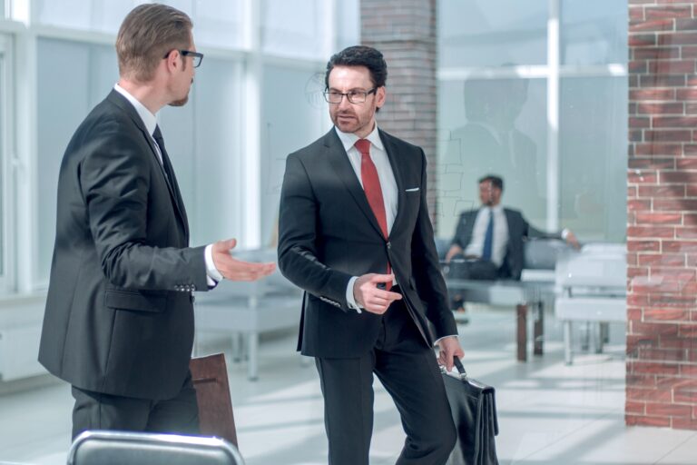 Business partners talking in the office hallway in the concept of 'How to Communicate an Office Move to Clients and Partners'.